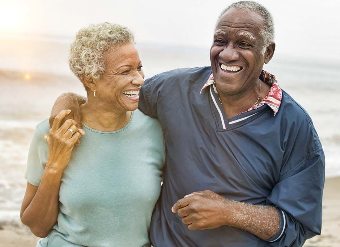 The Golden Years - Senior Couple Laughing and Embracing One Another While Walking along the Beach at Sunset